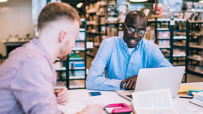 Two students work on a project in a library