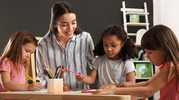 A teacher works with three students using colored pencils