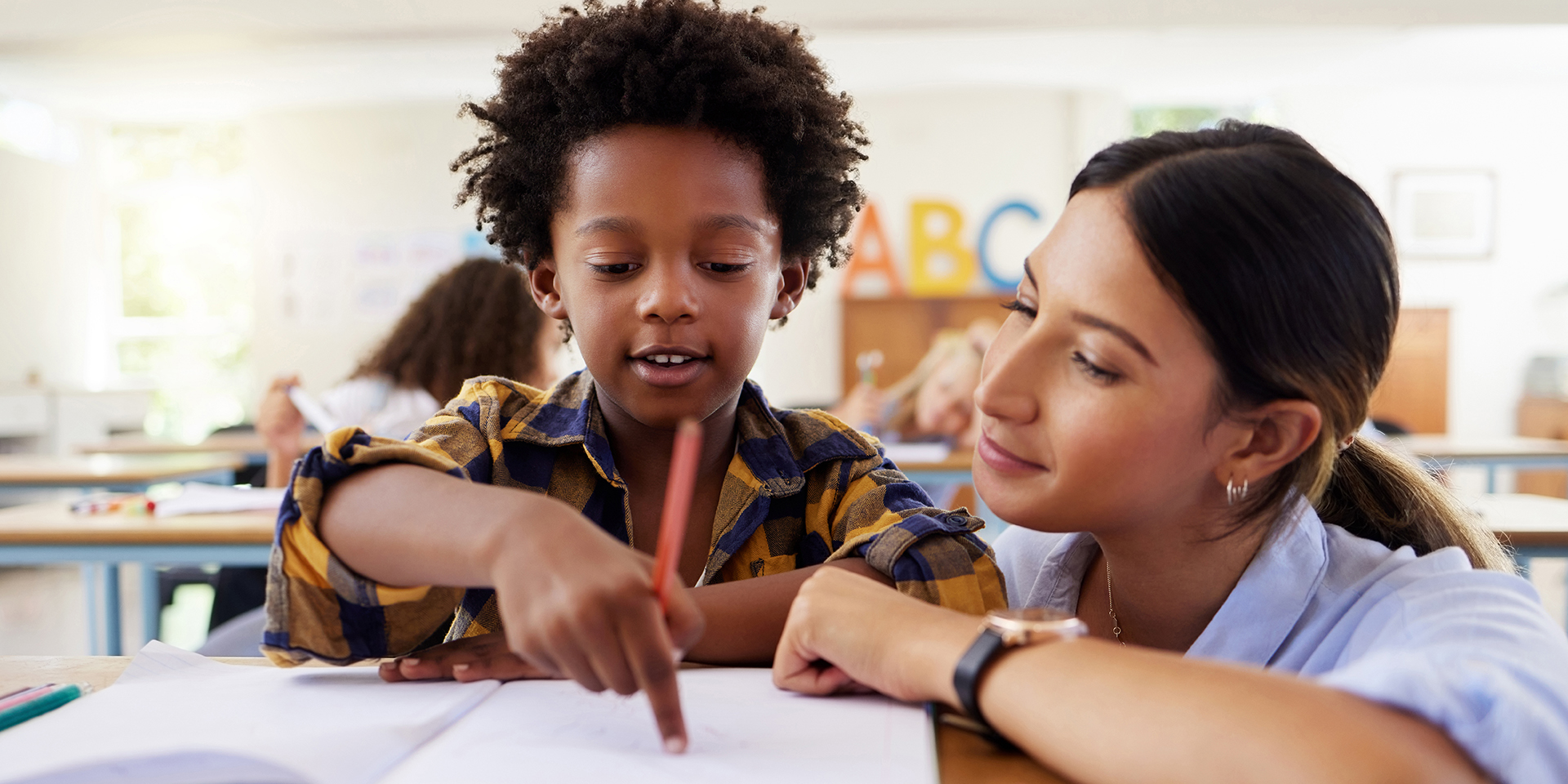 A teacher works with a student as he points out something in a book.