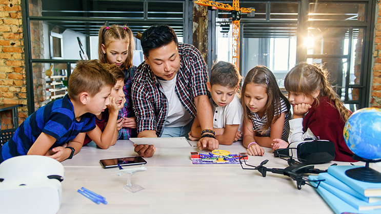 A teacher and group of students standing around a table.
