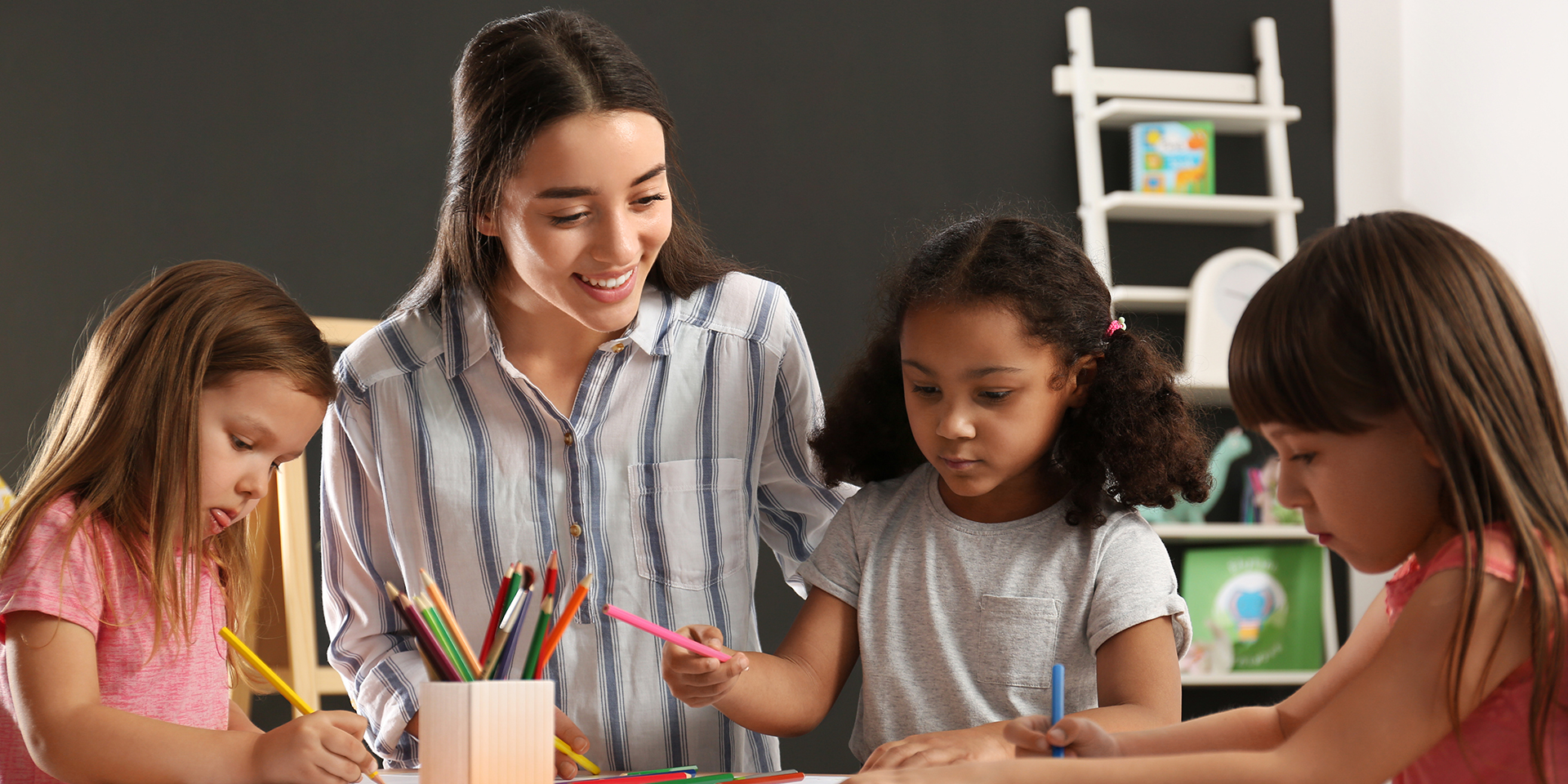A teacher works with three students using colored pencils.