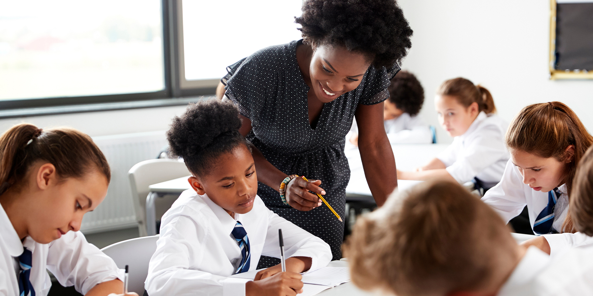 A female teacher points out something to a student over their shoulder.