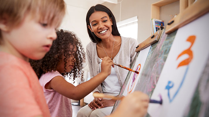 A teacher looks on as students paint on easels