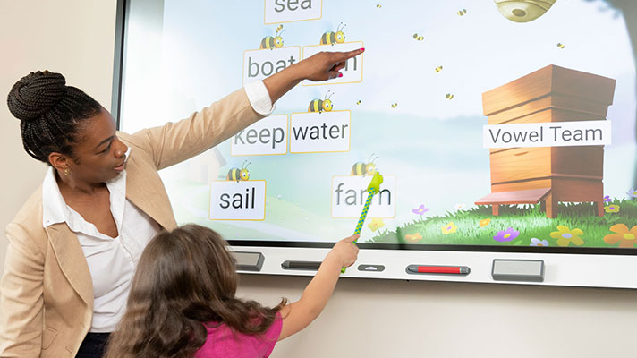 A teacher points out something to a student on a video board