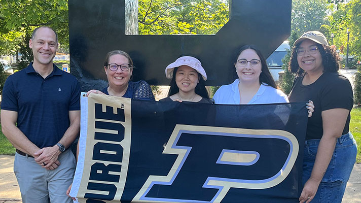 Purdue Higher Education PhD students stand in front of the large Purdue 
