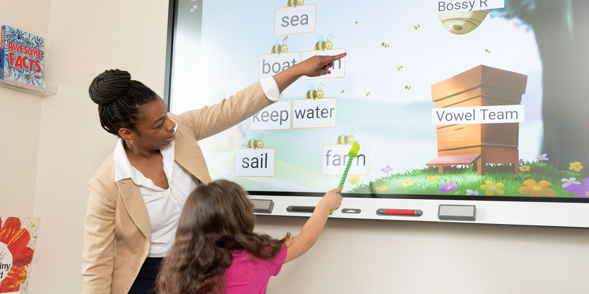 A teacher points out something to a student on a video board