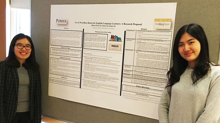 Two Purdue University students stand next to a poster during a research presentation