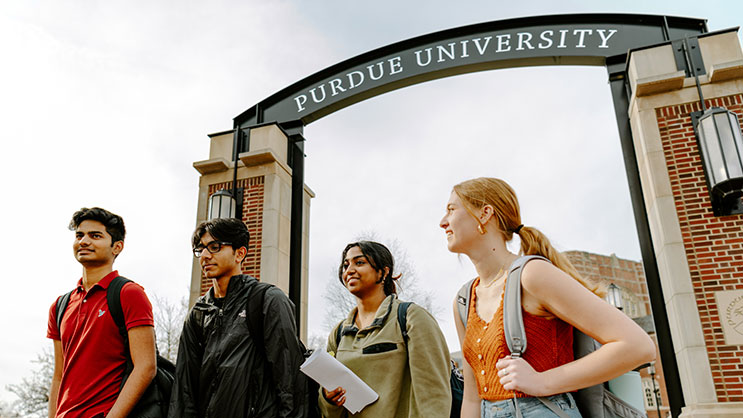 A group of four undergraduate students walking underneath the Purdue University arch.