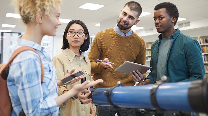 Three students and a teacher stand around a telescope discussing a project
