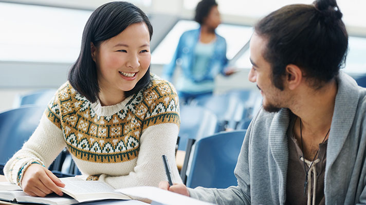 An Asian student looks at another student while going through some books