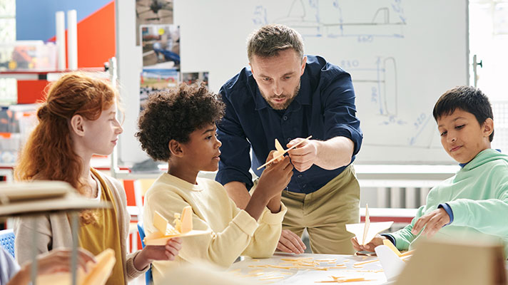 A teacher shows points out items on a model airplane to three students
