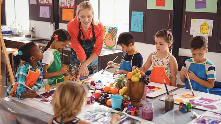 A female teacher works with students on an art project where they're painting