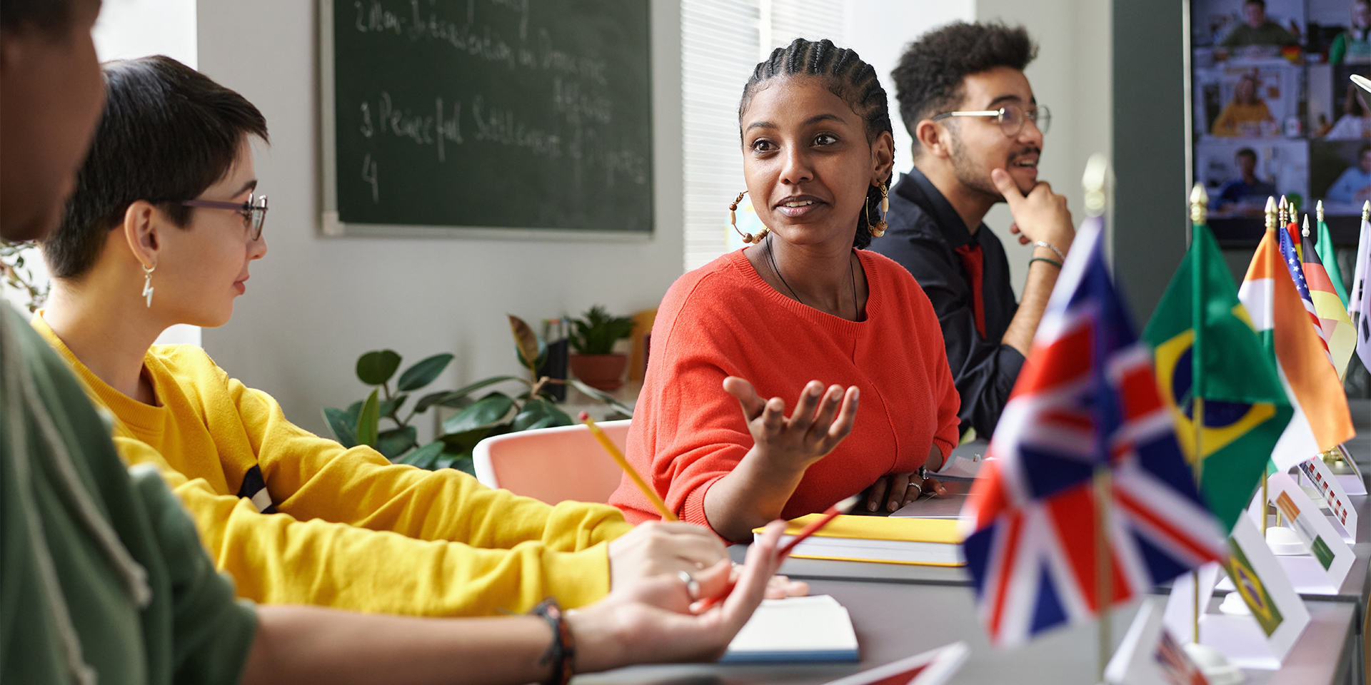 A student talks to other students during a project, different world flags are shown in the foreground