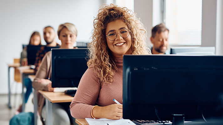 A female student works on a computer in a lab with other students