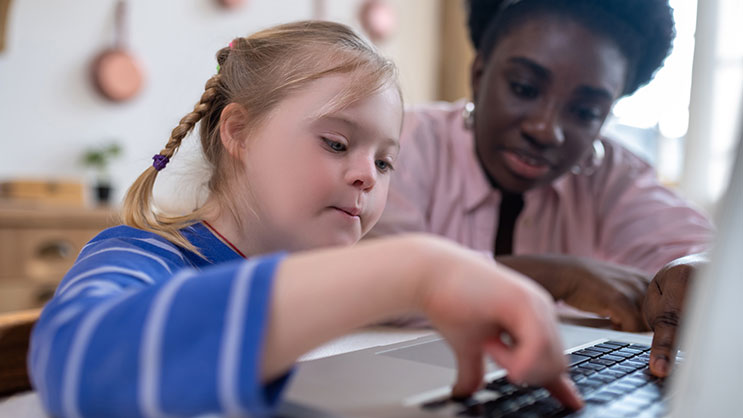 A teacher works with a student on a laptop