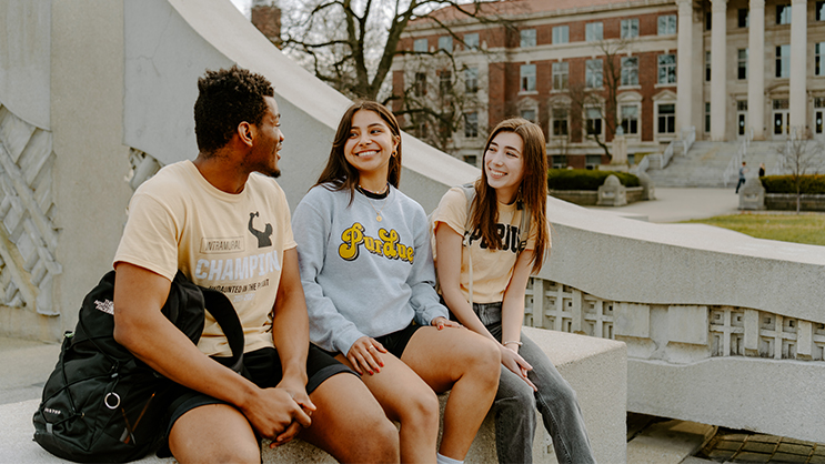 Three Purdue students sitting near a fountain. They are smiling and talking to each other.