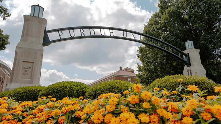 A ground level view of the Purdue University arch. In the foreground is a bush of orange flowers.