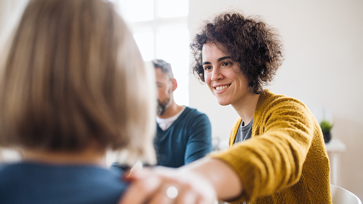 A young woman smiles and puts her hand on another woman's shoulder for support.