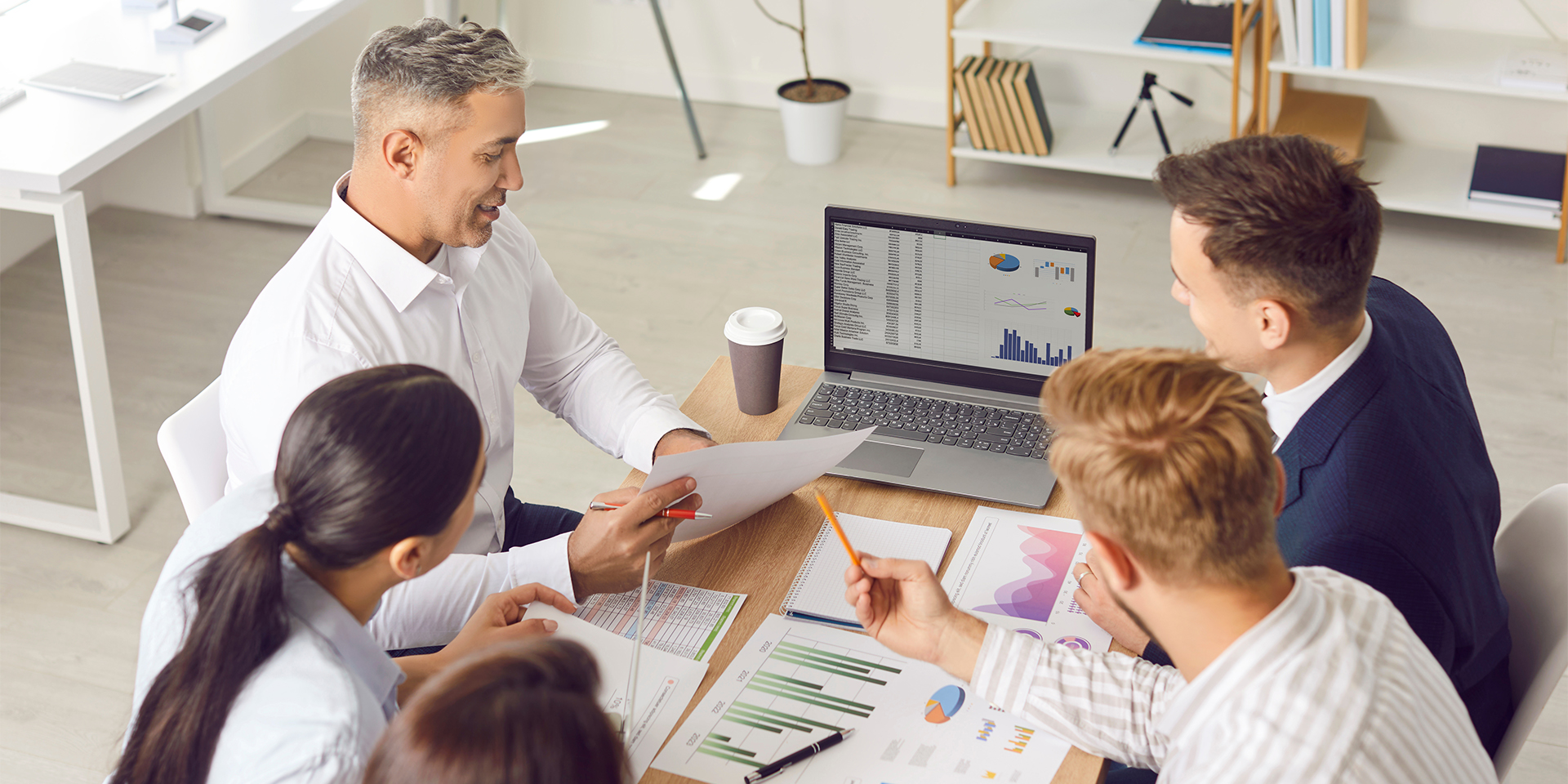 A team of business professionals seated a table with charts and graphs.
