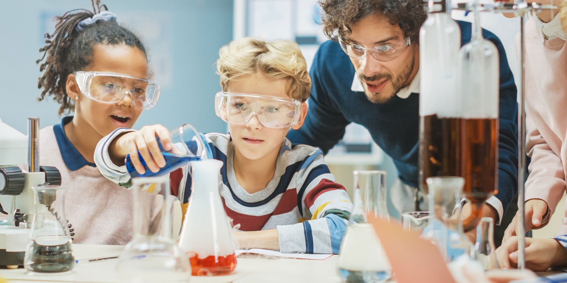 A male STEM teacher helps a group of students with a science experiment.