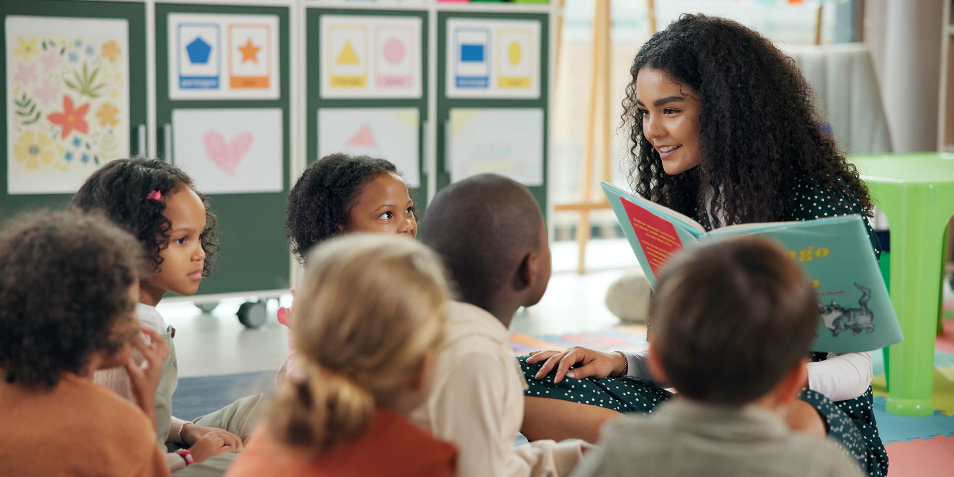 A female teacher reads a picture book to a group of young students