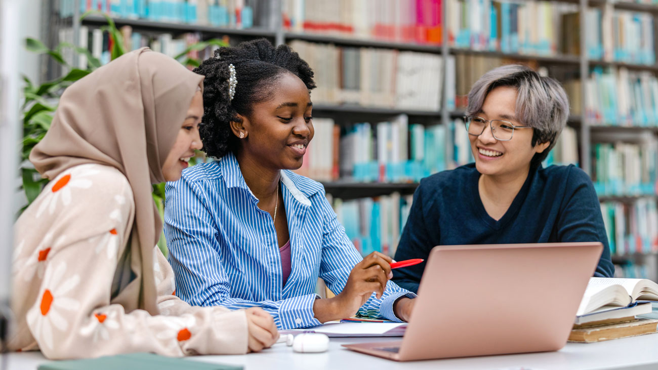 Three students work in a library around a computer
