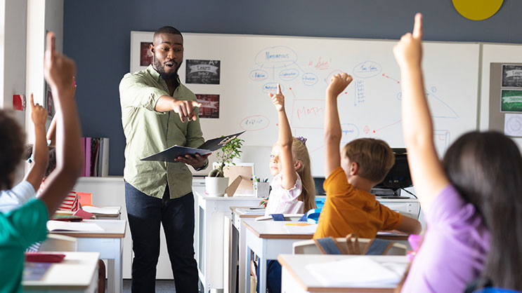 A black male teacher points to a student that has their hand raised in a classroom