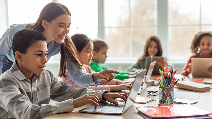 A female teacher works with students on laptops