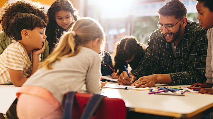 A male teacher works with a group of elementary students on an art project