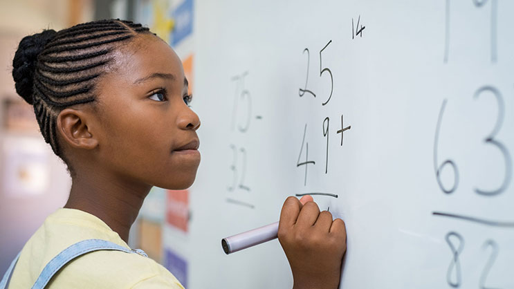 A young black female child works on a math problem on a whiteboard
