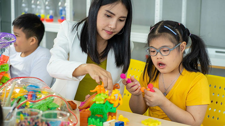 A female teacher works with a young student using blocks
