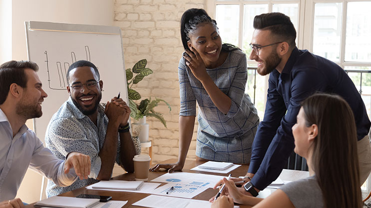 A group of people meet around a table discussing a presentation