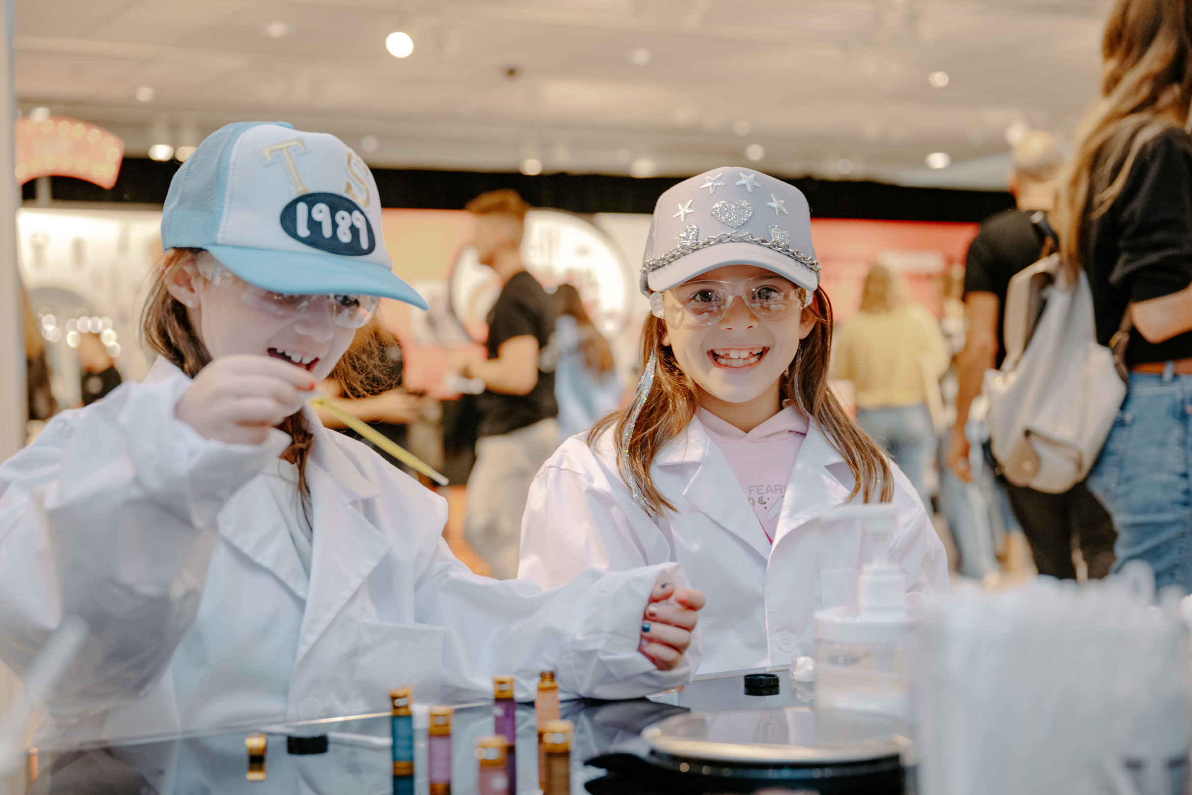 Two young girls performing a science experiment. They are wearing lab coats and safety goggles.