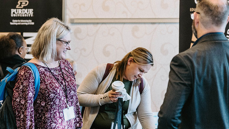 Two educators speak to a vendor at the Purdue AI in Education conference
