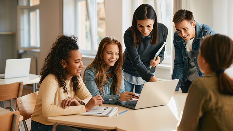 A group of high school students sitting at a desk around a laptop.
