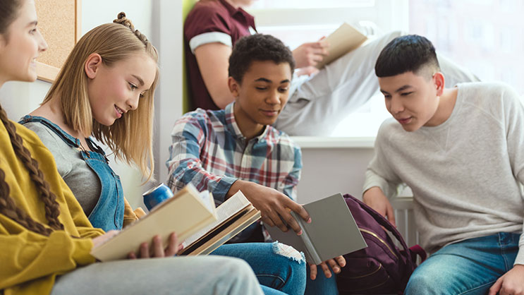 A group of high school students talking and reading books in a classroom.