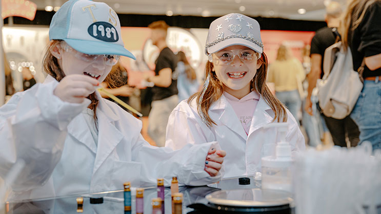 Two young girls in white lab coats work on a mixology experiment 