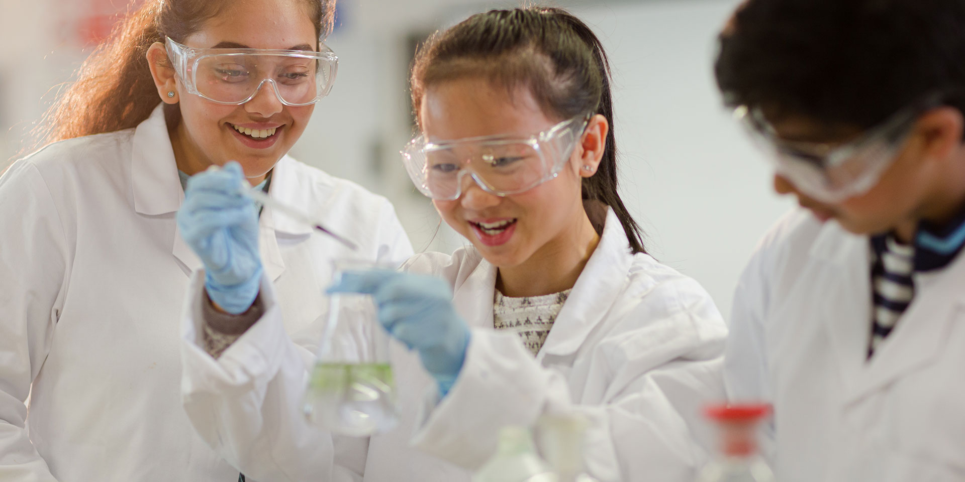 Three students in white lab coats work on an experiment