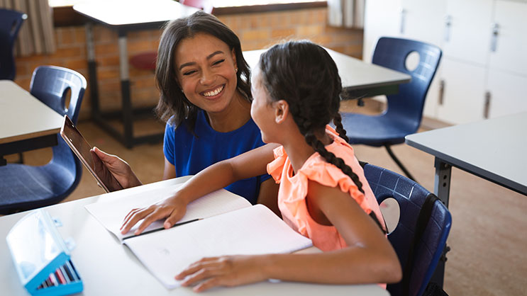 A student teacher bent over an elementary student's desk and smiling. 