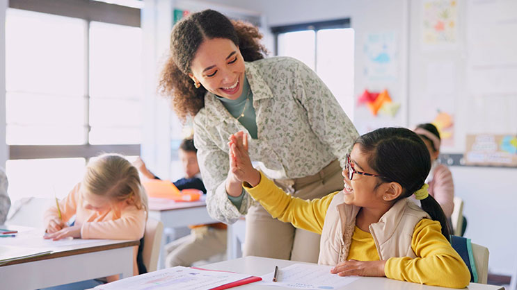A student teacher giving a high five to a young elementary student.