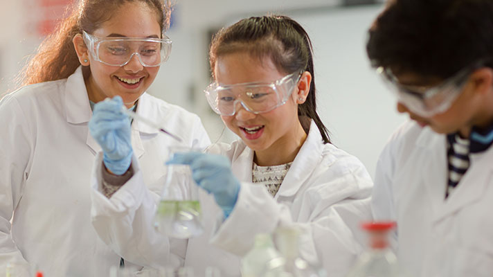 Three students in white lab coats conduct an experiment with beakers and liquid