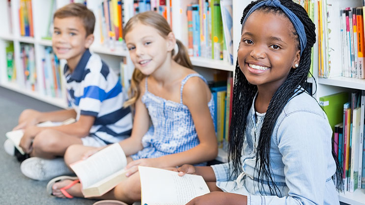 Three middle school students sit reading in a library
