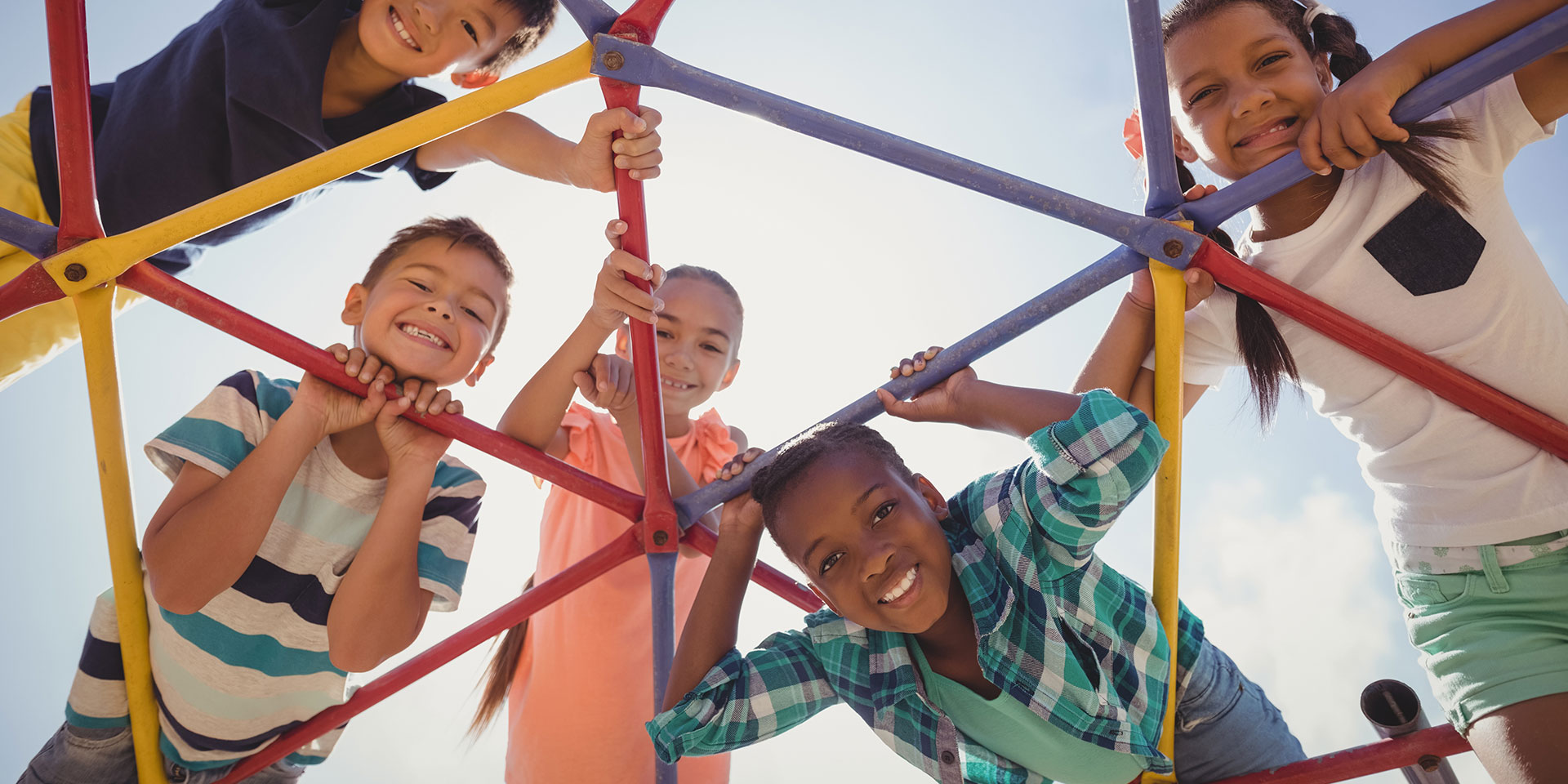 Students play on a jungle gym and look at the camera