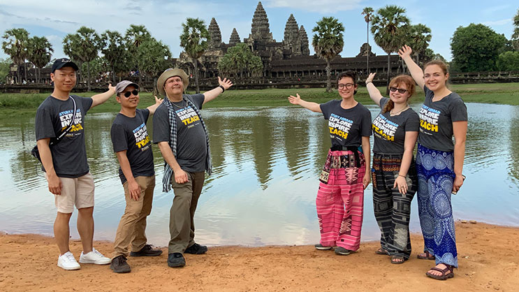 College of Education faculty and students posing for a photo in Cambodia. They each have one arm outstretched towards a landmark in the distance.