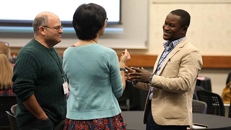 A black male presenter speaks with two conference attendees