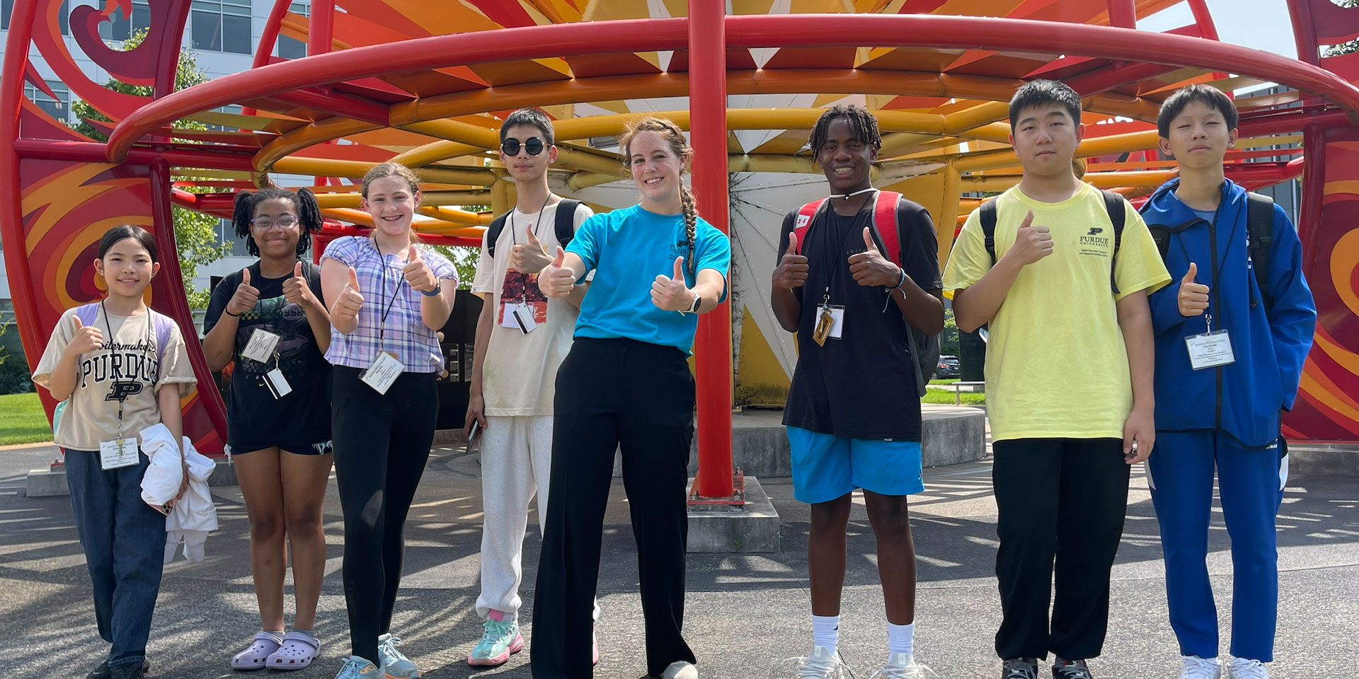 A group of GER2I Summer Residential campers stand in front of a sculpture on campus with their counselor.