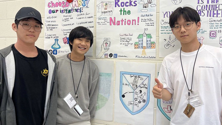 Three male GER2I Summer Residential campers stand in front their poster projects