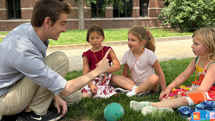 A GER2I Super Summer counselor speaks with a group of students outside while they sit in the grass