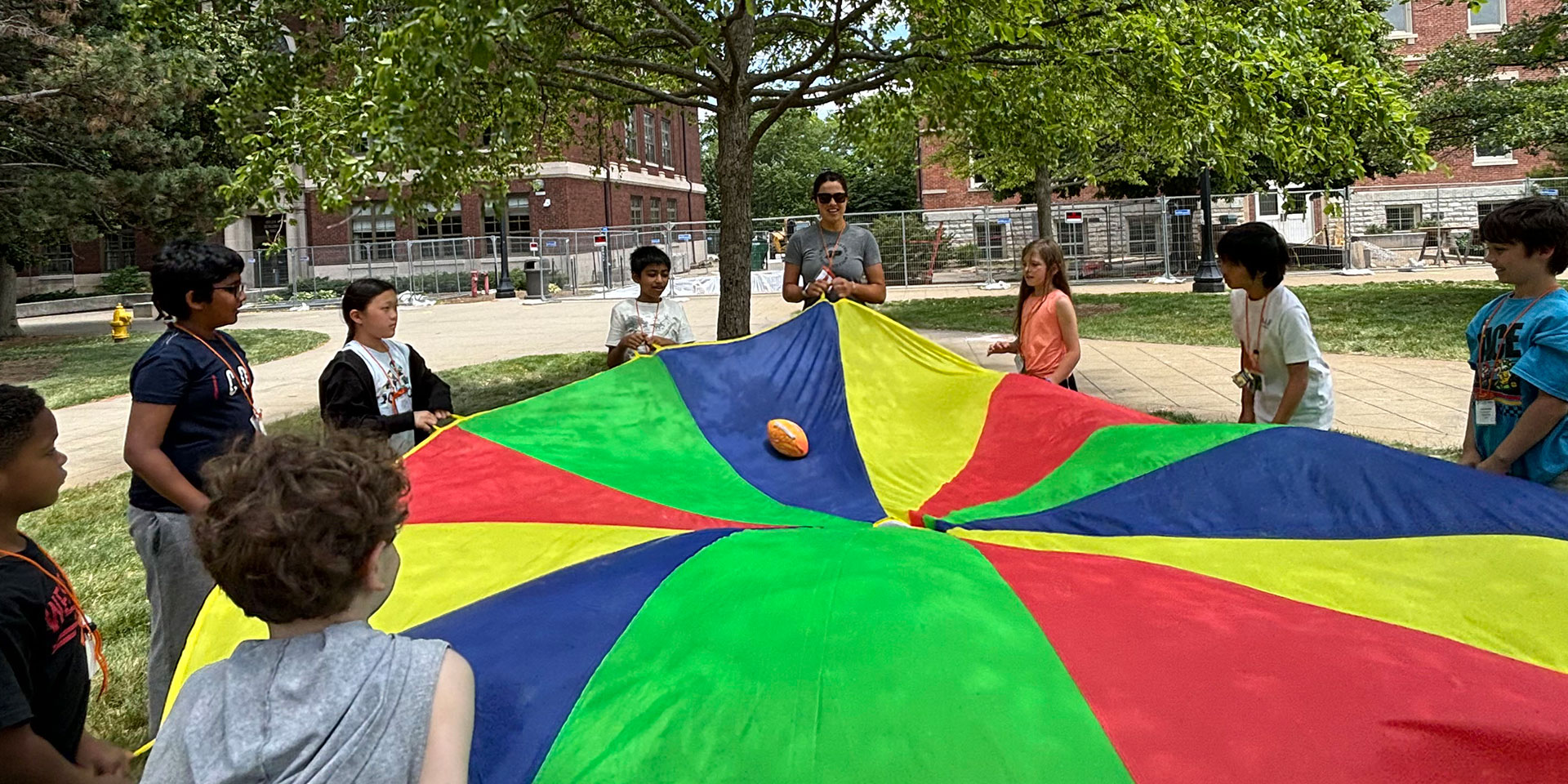 A group of young students at GER2I's Super Summer program do an activity with a parachute