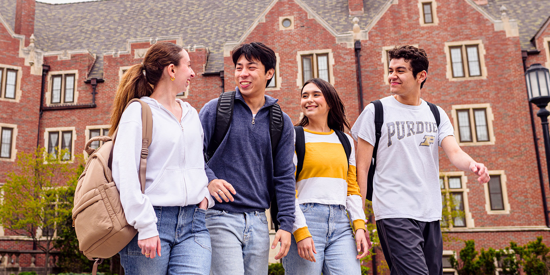A group of four Purdue students walking in front of a residential dorm.